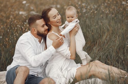 A joyful family with a baby relaxing outdoors in a field during summer.